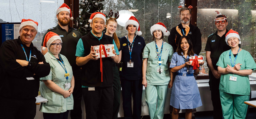 Some of the staff at Torbay Hospital wearing Christmas hats and holding gifts, standing by the tree in Bayview restaurant.