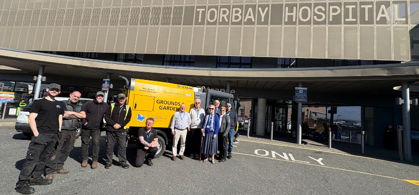Members of Torbay Hospital League of Friends and the gardens and grounds team standing in front of a roadsweeper.