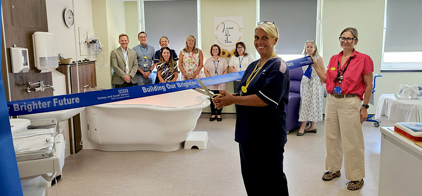 NHS staff members cut a blue ribbon reading "Building Our Brighter Future" to officially open The Cove birthing suite at Torbay Hospital, featuring a new white birthing pool in the background.
